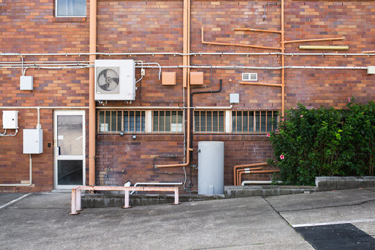 Rear exterior brick wall of commercial building with electrical panels, piping, and service door