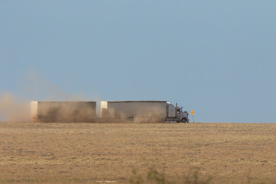 Heat ripples blurring prime mover pulling two curtain sided trailers on a dirt road