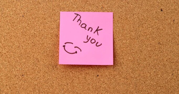 Pink sticky note paper with a handwritten Thank You message and a happy smiley face drawing, conveying positive emotion and appreciation message.