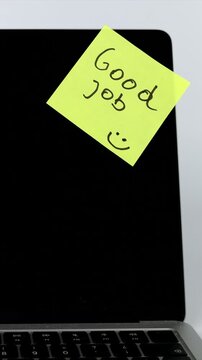 A close view of a hand attaching a yellow Good Job sticky note to a laptop screen, expressing appreciation, recognition, workplace positivity, motivation, and effective business communication.