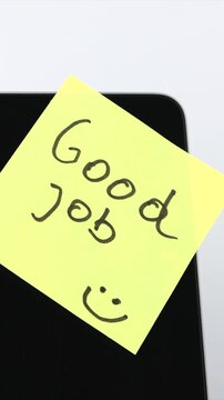 A yellow adhesive note with the words Good Job is carefully attached to a laptop display, symbolizing positive feedback, employee appreciation, workplace encouragement, and productive office communica