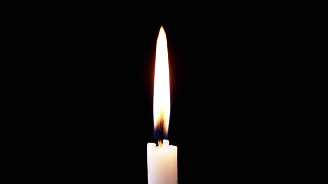 Isolated burning candle with bright flame on dark background with falling snow. One white wax candle with yellow flame illuminates particles of falling snow on black background. Concept of memory,