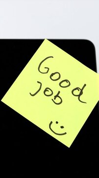 A hand places a yellow sticky note reading Good Job onto a laptop screen, creating a simple workplace motivation scene with appreciation, encouragement, recognition, and modern office inspiration.