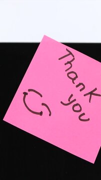A person attaches a bright pink adhesive memo note saying thank you to a clean computer screen in vertical frame showing corporate team gratitude.