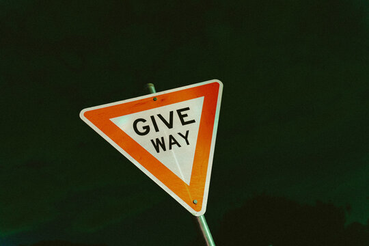 Triangular &ldquo;Give Way&rdquo; road sign stands against the dark