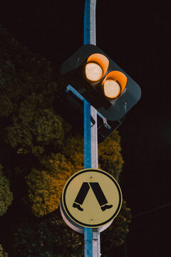 Amber traffic lights glowing above pedestrian crossing sign at night