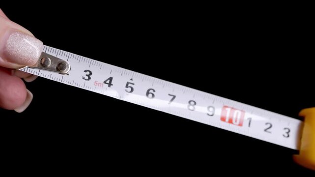 Hands pull a white measuring tape from a yellow plastic housing against a dark background. Concept of precision, diy home improvement, renovation, and construction measurement.