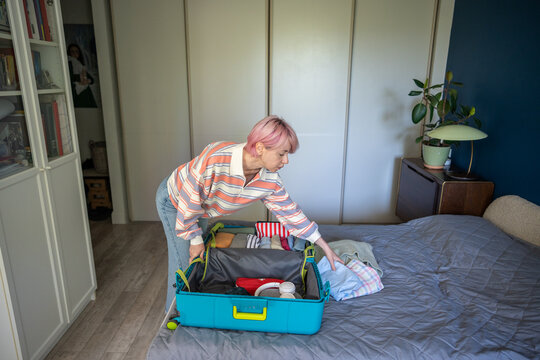 Mature woman tourist neatly arranging clothes and personal stuff in suitcase while preparing for trip, thoughtful female getting ready for holiday and packing belongings in travel case beforehand.