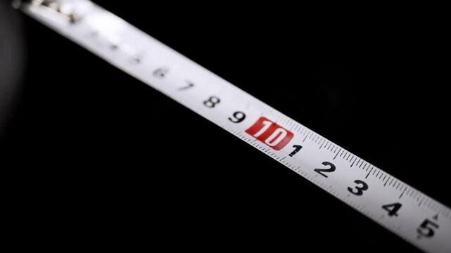 A white metallic measuring tape is illuminated against a dark background while subtle smoke drifts across the marked numbers. Concept of precision, measurement metrics, and exact dimensions.