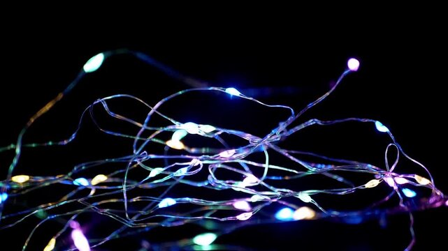 A tangled string of multi-colored LED fairy lights glows and shimmers against a dark, black background. Concept of festive decoration, holiday celebration, abstract technology, and vibrant ambiance