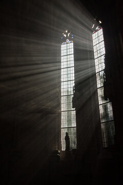 Sc&egrave;ne mystique dans une &eacute;glise catholique avec un halo de lumi&egrave;re des vitraux &eacute;clairant une statue et une bible