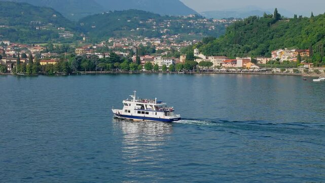 Ferry cruising along a town sector of Lake Garda, aerial view from drone. Public transport corridor reducing road congestion between lakeside towns