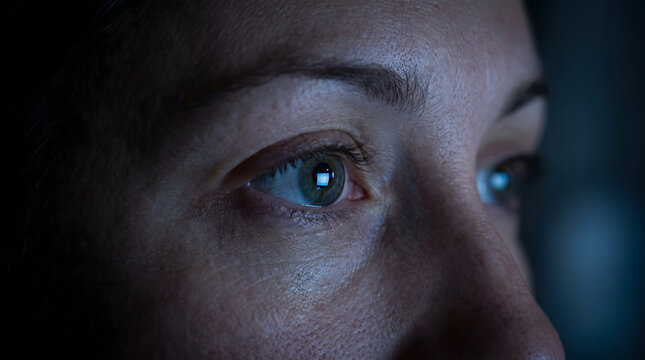Doomscrolling concept close up woman eye glowing from mobile phone display light reading bad news in bed at midnight