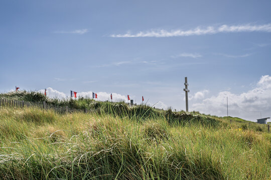French flags and the Cross of Lorraine monument on a grassy hill overlooking the sandy shore of Juno Beach in Courseulles-sur-Mer Normandy France historic WW2 site.