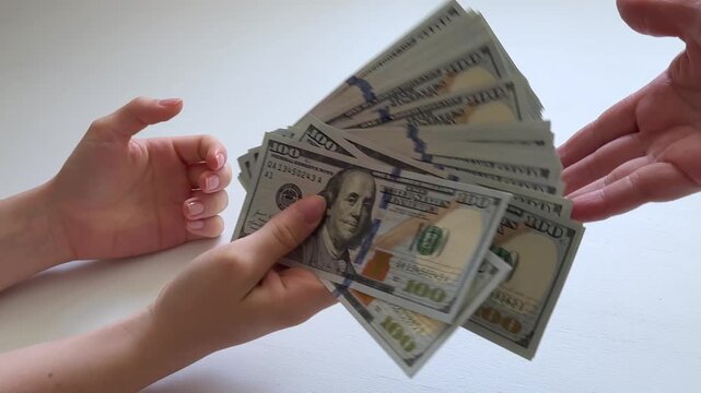 100 dollar banknotes is passed between two women, but only part of the cash is received while remaining bills fall. Concept of money loss, payment mistakes, financial risk and failed cash transfer.