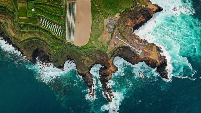Ocean waves break inside rocky inlet below basalt cliffs on Azores Island. Atlantic wave activity, white sea foam and turbulent water