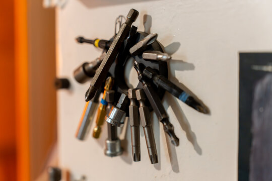 Collection of various interchangeable screwdriver bits, torx bits, and hex sockets attached to a round magnetic tool holder on a wall inside a workshop.