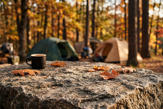 Rough natural stone surface covered in dry autumn leaves with camping tents blurred in distance