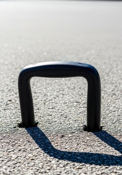 A closeup of a black plastic luggage handle warping and sagging under intense solar heat on a bright outdoor asphalt ground during summer, climate, gear, sun