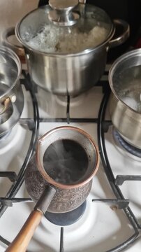 Dark Turkish coffee steams in an ornate copper pot while rice boils on a busy kitchen gas stove. Concept of authentic home cooking, morning routines, and culinary multitasking.
