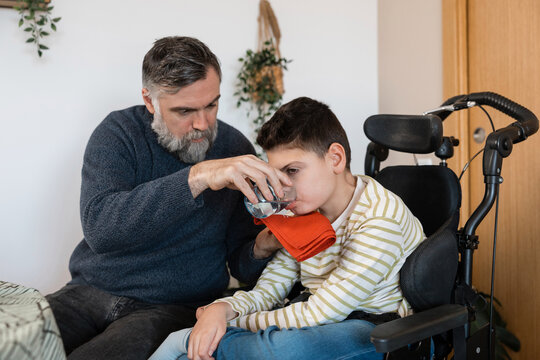 Father helping boy with cerebral palsy drink water