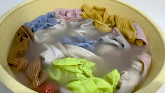 Colorful socks soaking in yellow basin with soapy water, hand washing laundry at home, various bright and pastel colored clothing items being cleaned, household chore, cleaning concept
