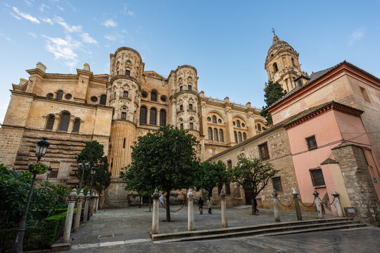 Low angle perspective of the majestic facade and bell tower of the Malaga Cathedral (Catedral de la Encarnaci&oacute;n) under a partly cloudy sky, from a quiet square.