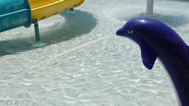 Close up view of dolphin water fountain beside colorful waterslide in shallow family resort splash pool. Crete. Greece.