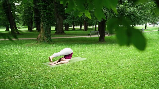 Woman practicing yoga in serene forest doing Plough Pose and Urdhva Mukha Paschimottanasana stretch on green lawn. Peaceful environment for focus and connection with nature in outdoor setting. 4K