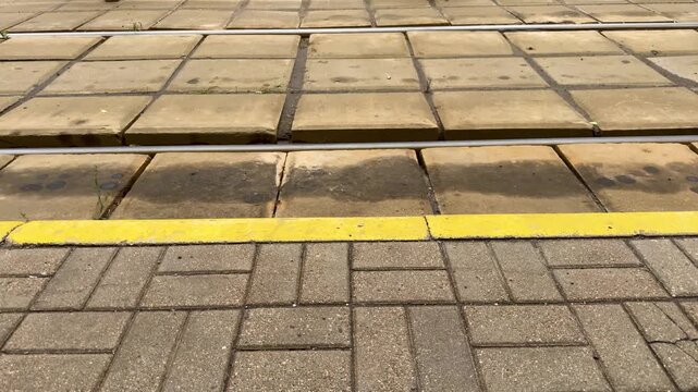Tram tracks and platform edge with yellow safety line. Concrete slabs and paving stones at urban transport stop, railway infrastructure, city transit