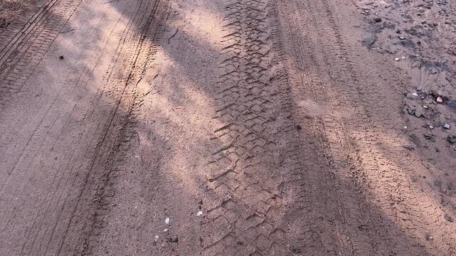 Tire tracks on a sandy dirt road with tree shadows, rough off-road terrain texture, outdoor background, vehicle path, nature surface