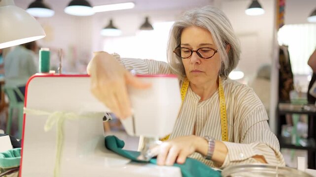 Mature female tailor sewing clothes in workshop