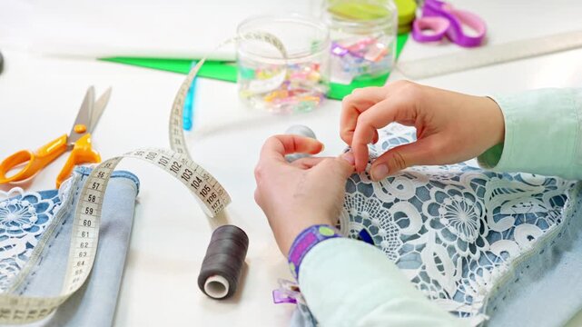 Seamstress hand sewing lace on denim fabric