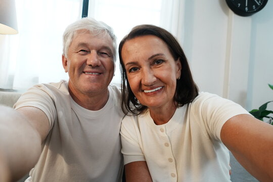 The grandparents are holding their smartphones, taking selfies and smiling at the camera together.
