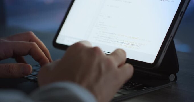 Close-up of hands typing on a tablet keyboard with lines of code visible on the bright screen.