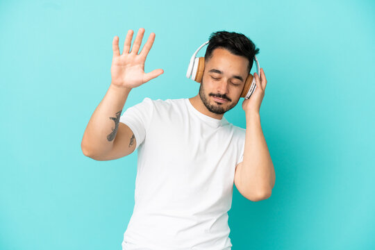 Young caucasian man isolated on blue background listening music and dancing