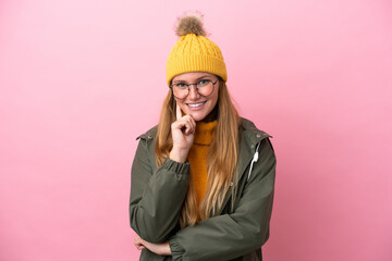 Obraz premium Young blonde woman wearing winter jacket isolated on pink background with glasses and smiling