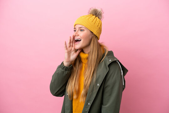 Young blonde woman wearing winter jacket isolated on pink background shouting with mouth wide open to the lateral