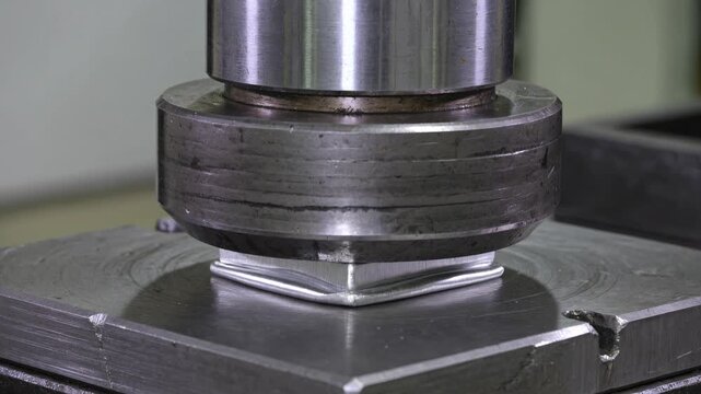 Hydraulic press machine crushing and deforming a shiny metal cube during a strength and durability test in an industrial laboratory showing material resistance and pressure