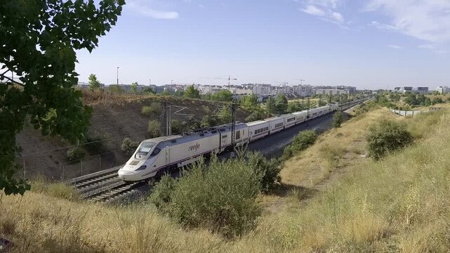 High speed passenger train crossing the Madrid suburban landscape under a clear blue summer sky