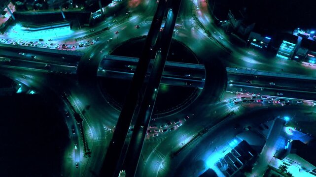 Brightly illuminated expressway traffic flows in this aerial view capturing dynamic night scene of vehicles moving along busy motorway interchange within an urban cityscape, highlighting significant r