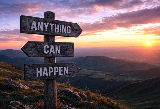 Inspirational wooden signpost with anything can happen message at sunrise over scenic mountain landscape