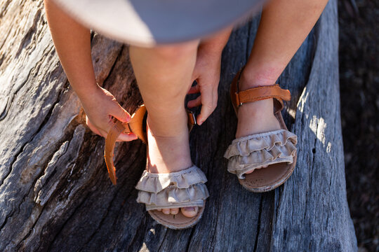 Child doing up buckles on sandal shoes while sitting on log outdoors