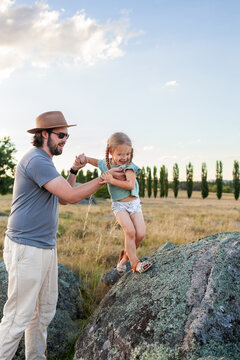 Dad helping daughter climb lichen covered boulders in soft sunset light