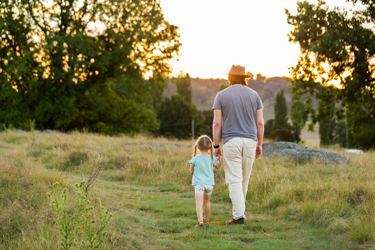 Dad on walk with young daughter walking away down grassy path in recreational area