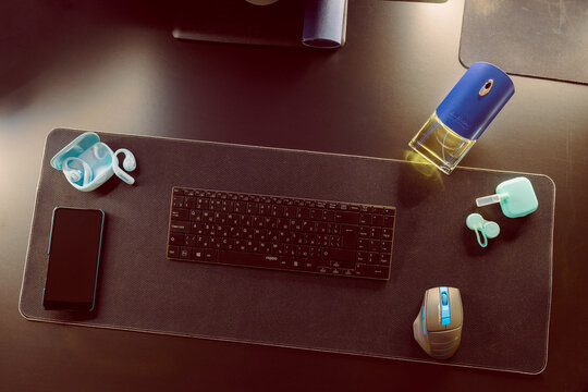 KYIV, UKRAINE - November 29, 2026: A Givenchy perfume bottle and turquoise Anker headphones with a case arranged near a keyboard, smartphone, and contact lens containers on a black desk mat.