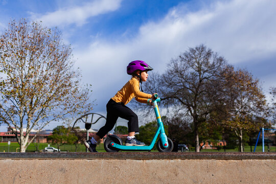 Child riding scooter at skate park wearing purple helmet