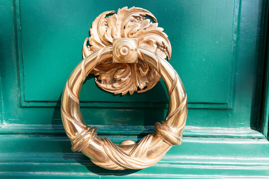 Ornate bronze door knocker on a teal-green Parisian door, featuring acanthus leaf design and twisted ring handle.