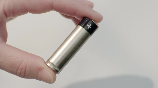 Human hand holding cylindrical AA battery with fingers close-up