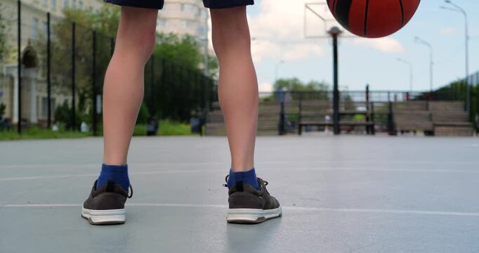 Young athlete prepares for basketball game on court. Player dribbles basketball, showcasing skills and focus. Outdoor sports environment creates energetic atmosphere